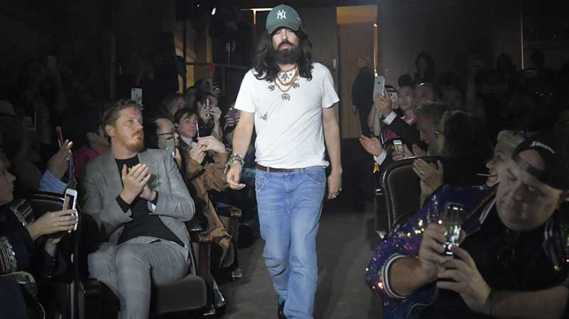 Alessandro Michele im weißen T-Shirt, Jeans und grüner Baseballcap mit mehreren Layering-Ketten beim Schlussgang einer Gucci-Show, applaudierendes Publikum