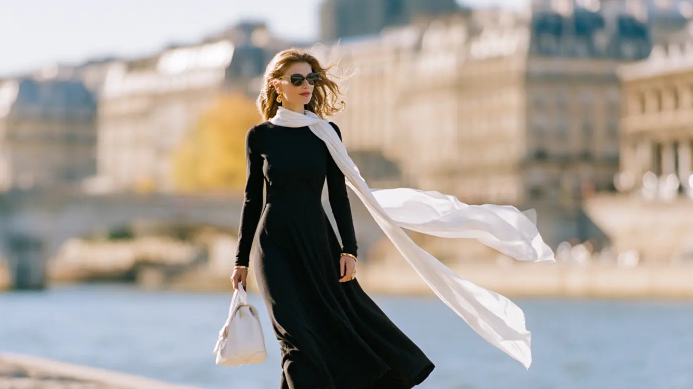 Frau im schwarzen Langarm-Midikleid mit wehendem weißem Seidenschal am Seine-Ufer in Paris – KI-Illustration