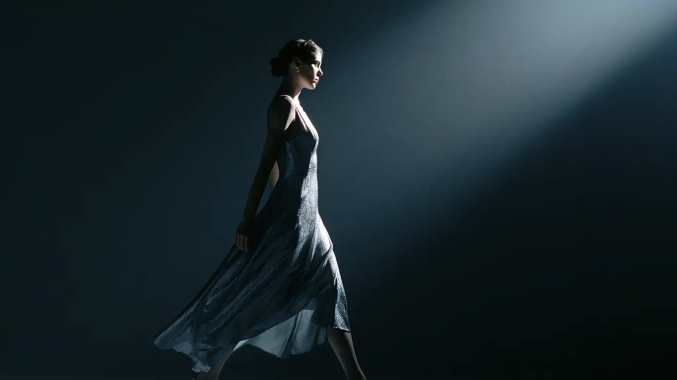 Frau im schimmernden silbernen Kleid im Lichtstrahl eines Spotlights vor dunklem Hintergrund – KI-Illustration