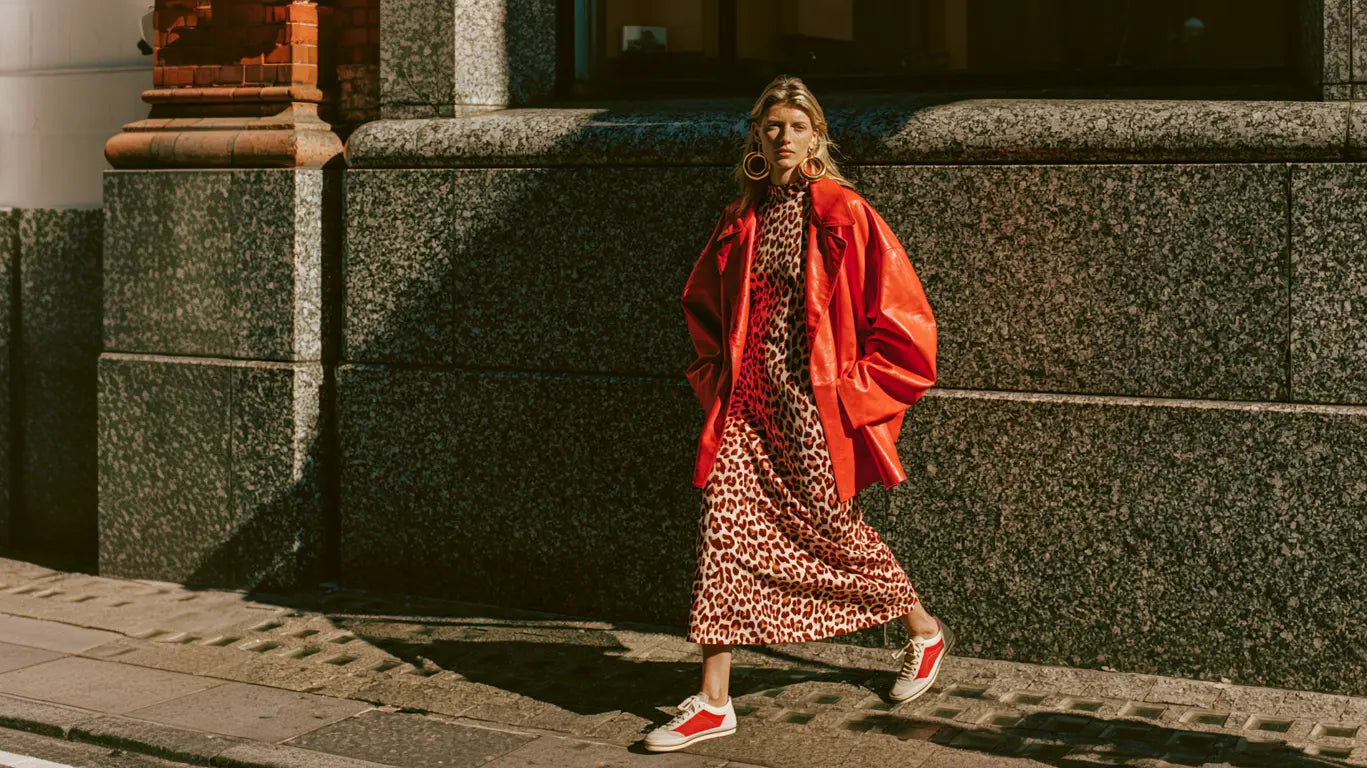 Frau im Leo-Midikleid mit rotem Lederblazer und Sneakern auf sonniger Straße – KI-Illustration