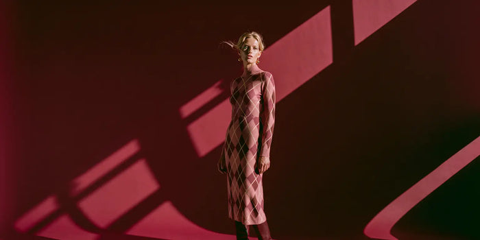 Frau im taillierten Argyle-Strickkleid in Blush, Mauve und Braun vor tiefrotem Hintergrund – KI-Illustration