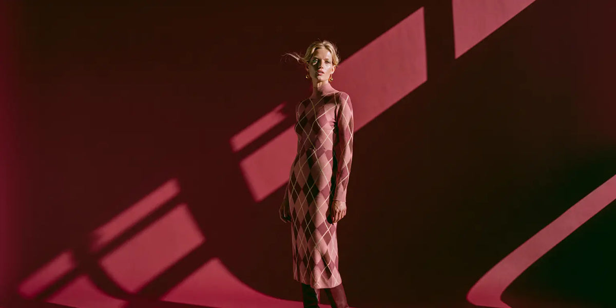 Frau im taillierten Argyle-Strickkleid in Blush, Mauve und Braun vor tiefrotem Hintergrund – KI-Illustration