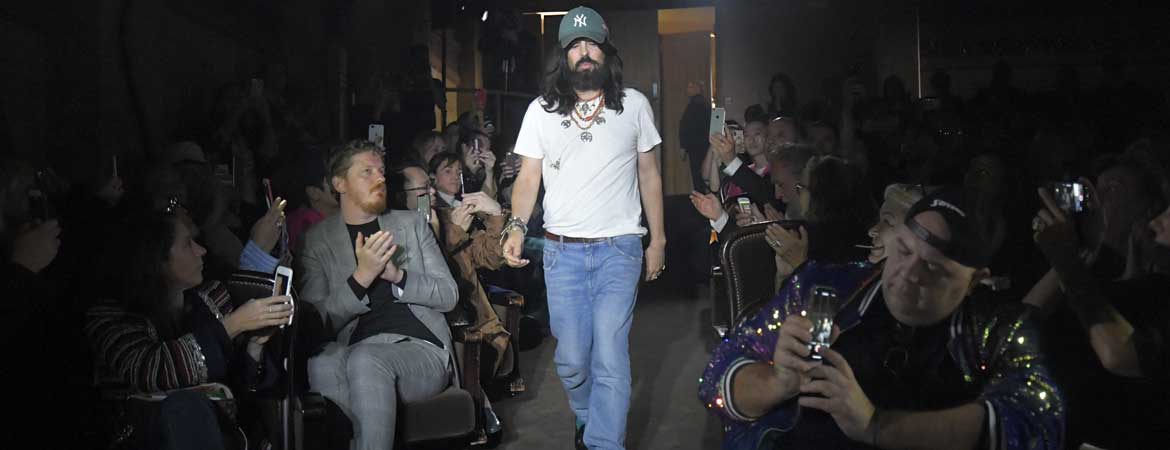 Alessandro Michele im weißen T-Shirt, Jeans und grüner Baseballcap mit mehreren Layering-Ketten beim Schlussgang einer Gucci-Show, applaudierendes Publikum