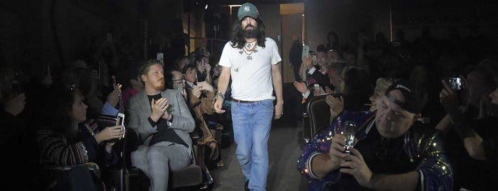 Alessandro Michele im weißen T-Shirt, Jeans und grüner Baseballcap mit mehreren Layering-Ketten beim Schlussgang einer Gucci-Show, applaudierendes Publikum