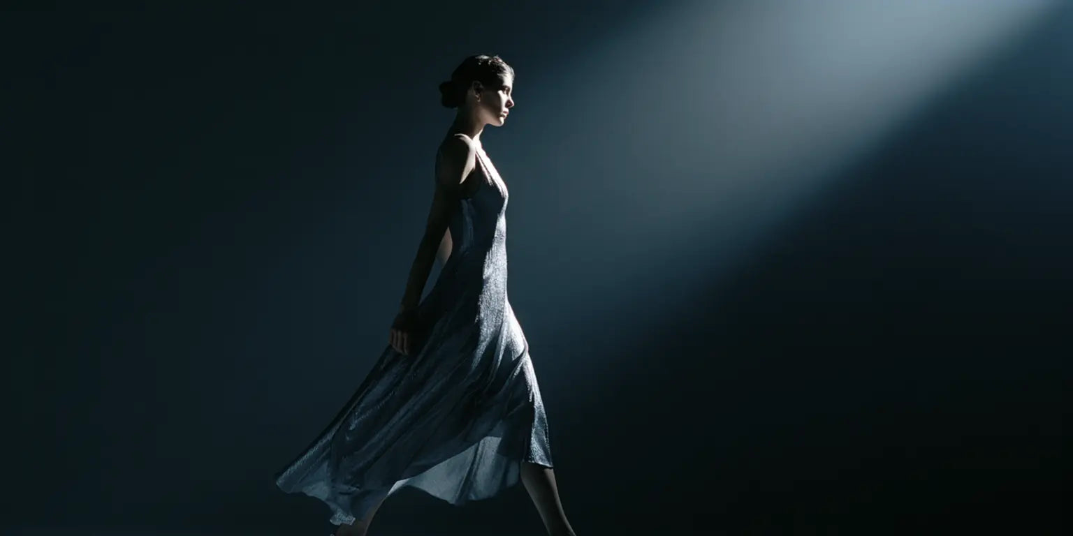 Frau im schimmernden silbernen Kleid im Lichtstrahl eines Spotlights vor dunklem Hintergrund – KI-Illustration